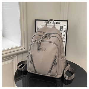 Detail of grey lychee leather backpack showing round logo and metal bell charm