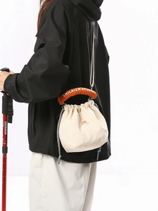 Outdoor style cream drawstring bucket bag with orange handle shown on a model