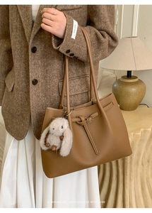 Close-up of brown pebbled leather tote bag with decorative belt and plush rabbit charm