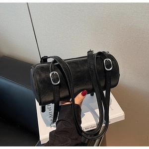 Detail of black cylindrical shoulder bag featuring retro leather texture and silver buckles