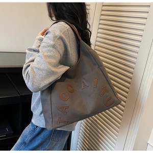 Detail of grey canvas tote bag featuring brown leather letter patch and premium texture