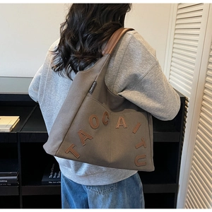 Detail of grey canvas tote bag with leather letter patch shown in a lifestyle setting