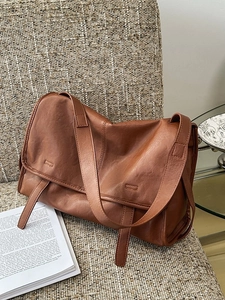 Vintage brown leather messenger bag with wide strap on a chair in a cozy lifestyle setting