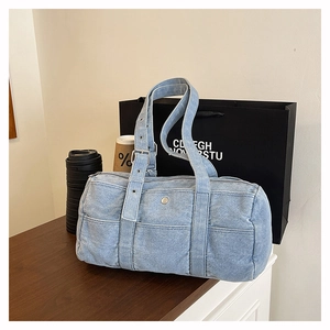 Detail of light blue denim barrel bag featuring white stitching and adjustable strap