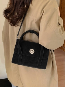 Chic black faux suede crossbody bag with metal lock worn by model in trench coat