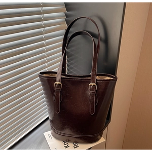 Detailed close-up of dark brown oil-wax leather texture and gold buckles on a bucket bag