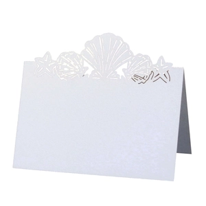 Detailed laser-cut seashell and starfish design on a white pearlescent wedding place card