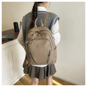 Close-up of khaki pebbled leather backpack with multi-layer zippers and embossed logo detail