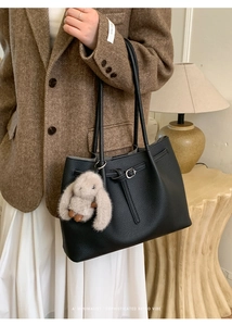 Close-up of black lychee grain leather tote bag with cute plush rabbit charm detail