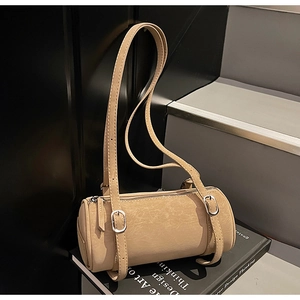 Detail of a beige cylinder shoulder bag with silver buckles on a modern staircase