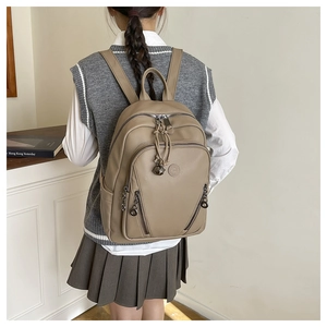 Detail of khaki leather backpack with embossed logo and bell charm on a model's back