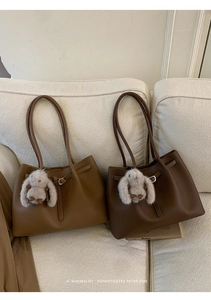 Detailed view of brown lychee texture tote bags with plush rabbit charms on a white sofa