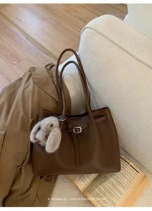 Brown leather tote bag with a plush rabbit charm shown in a cozy aesthetic setting