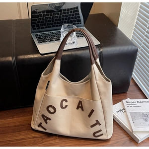 Close-up of canvas tote bag showing brown leather letter patches and quality stitching