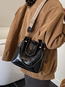 Vintage glossy black bucket bag with a wide patterned shoulder strap and gold accents