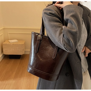 Detail of dark brown leather bucket bag with glossy wrinkled texture and adjustable strap