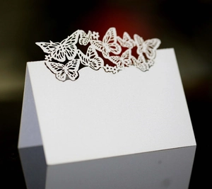 Elegant white laser-cut butterfly place cards made of pearl paper on a black mirror surface