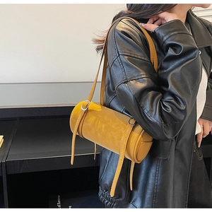 Detailed shot of yellow cylinder shoulder bag with adjustable straps on leather jacket