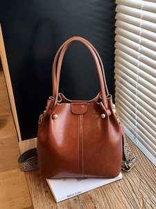 Vintage brown leather bucket bag with top handles and a colorful woven shoulder strap