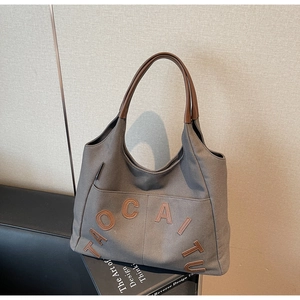 Detail of grey canvas tote bag featuring brown leather handles and 3D letter applique