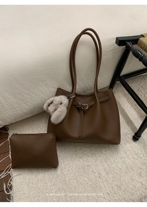 Minimalist brown leather tote and pouch set with a plush rabbit charm in a home setting