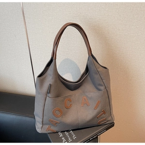 Macro view of dark grey canvas tote bag with brown leather handles and letter patch