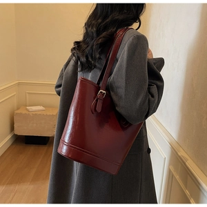 Detail view of burgundy leather bucket bag styled with a minimalist grey blazer outfit