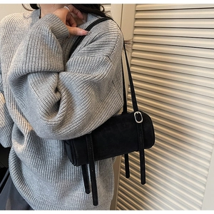 Close-up of minimalist black matte cylinder bag with thin shoulder straps on a gray sweater