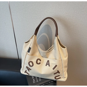 Close-up of beige canvas tote bag with brown leather handles and brand logo detail