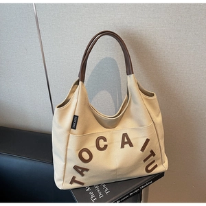 Detail view of large canvas tote bag with leather handles and letter decoration