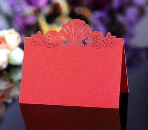 Macro detail of red laser-cut wedding place card with seashell and starfish design