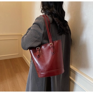 Detail of burgundy bucket bag featuring glossy leather texture and gold buckle accents