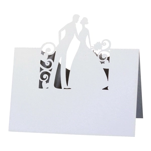 Close-up of white laser-cut wedding place card featuring bride and groom silhouette design