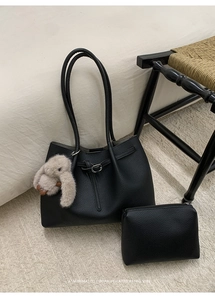 Close-up of black litchi grain tote bag set with plush rabbit charm on a woven chair