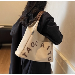 Detail shot of canvas tote bag showing the TAOC AITU vintage lettering and brown handle