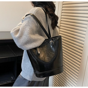 Detail of glossy black bucket bag with adjustable shoulder straps on model's shoulder