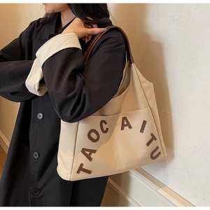 Close-up of beige canvas tote bag with brown leather handles and large front pocket detail
