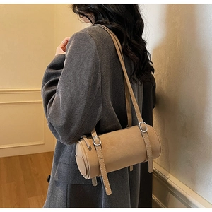 Detail shot of a beige cylindrical shoulder bag featuring buckle straps on a model