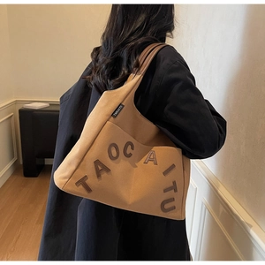 Detailed back view of a camel canvas tote bag with letter patches shown on a model