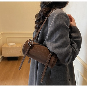 Detail view of brown cylinder shoulder bag with adjustable strap worn by a model in a suit