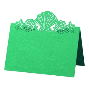 Detailed laser cut sea shell and starfish design on green folding wedding table card