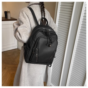 Detail of black litchi grain leather backpack with silver zippers on a casual model