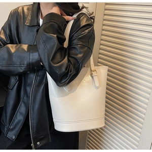 Close-up of white glossy bucket bag with gold hardware worn by a model in a leather jacket