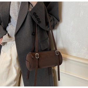 Detail of a dark brown cylinder bag with matte leather and adjustable shoulder straps