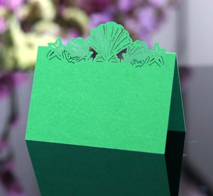 Detailed laser-cut green place card with intricate seashell and starfish hollow design
