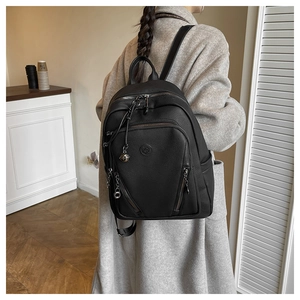 Detail of black pebbled leather backpack showing circular logo and metallic charm on zippers