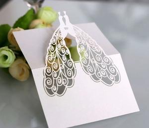 Macro shot of laser-cut white pearl paper wedding place cards with peacock design