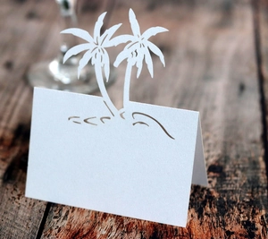 Detail of white laser-cut palm tree place card on a rustic wood background for weddings