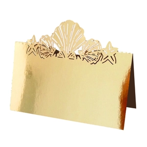 Detail of laser-cut gold wedding place card with seashell and starfish hollow design
