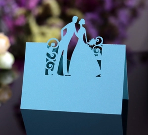 Close-up of light blue laser-cut wedding place card featuring a romantic couple silhouette